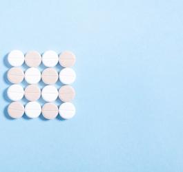 Białe i różowe tabletki ułożone w kształt kwadratu na błękitnym tle.