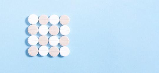 Białe i różowe tabletki ułożone w kształt kwadratu na błękitnym tle.