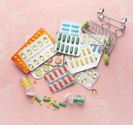 Przewrócony, zabawkowy wózek sklepowy, a w nim blistry różnych tabletek i kapsułek.