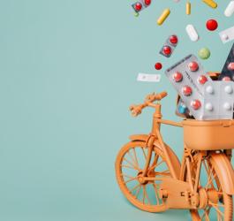 Pomarańczowy, zabawkowy rower przewozi rozmaite leki w tylnym koszyku.