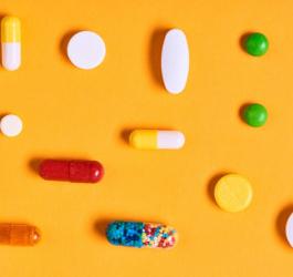 Białe i kolorowe tabletki oraz kapsułki na żółtym tle.