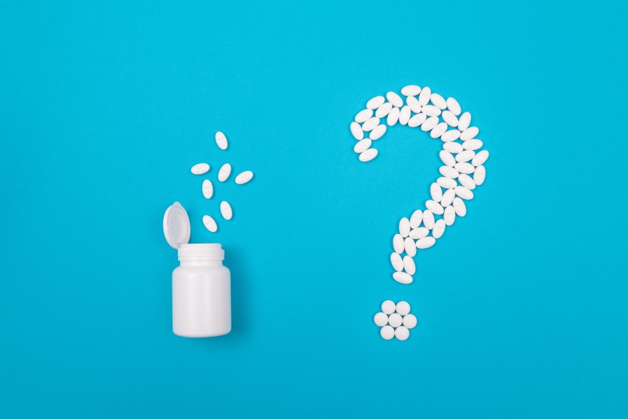 Biała buteleczka i białe tabletki ułożone w kształt znaku zapytania.