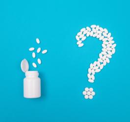 Biała buteleczka i białe tabletki ułożone w kształt znaku zapytania.
