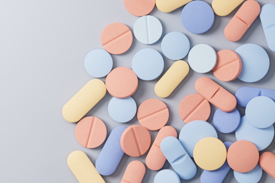 Kolorowe, pastelowe leki rozsypane na szarym tle.