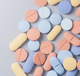 Kolorowe, pastelowe leki rozsypane na szarym tle.