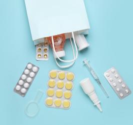 Blistry leków, syrop, aerozol i zastrzyk wysypane z torebki na zakupy.