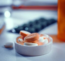 Białe i pomarańczowe tabletki w nakrętce po butelce leku, w tle blistry leków.