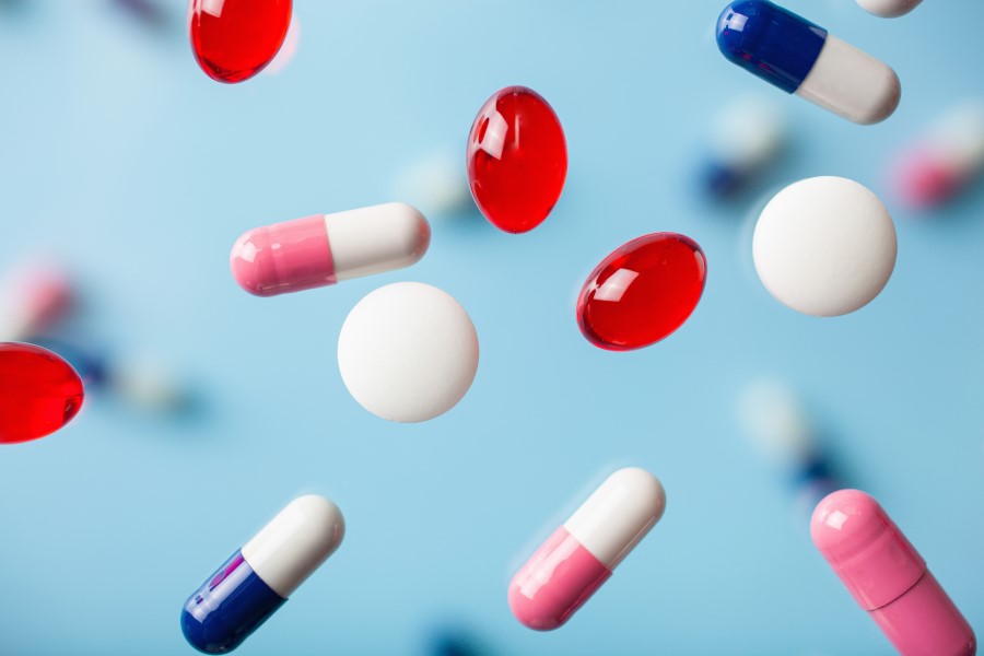 Tabletki i kolorowe kapsułki na niebieskim tle.