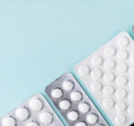 Szare i białe blistry leków na turkusowym tle.