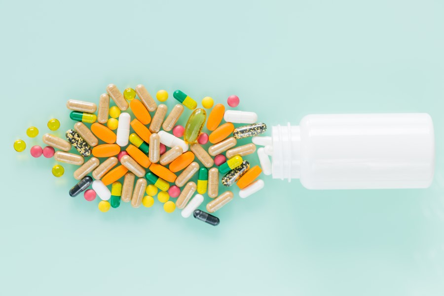 Biała buteleczka z której wysypują się różnobarwne leki.