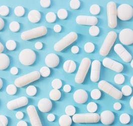 Białe tabletki i kapsułki rozsypane na błękitnym tle.