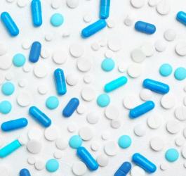 Białe tabletki oraz niebieskie tabletki i kapsułki rozsypane na białym tle.