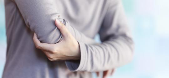 Kobietę boli łokieć, cierpi na łokieć golfisty.