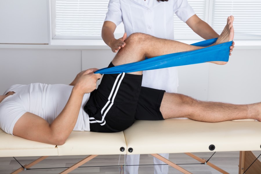 Mężczyzna w trakcie rehabilitacji wykonuje ćwiczenia pod okiem rehabilitantki.