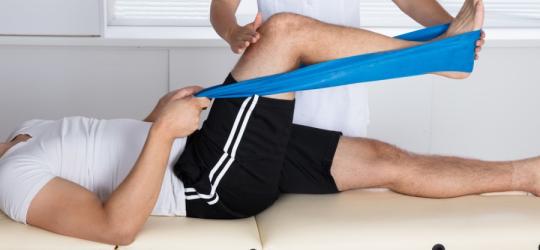 Mężczyzna w trakcie rehabilitacji wykonuje ćwiczenia pod okiem rehabilitantki.