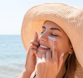 Kobieta na plaży nakłada na skórę twarzy krem ochronny.