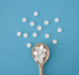 Białe tabletki na drewnianej łyżce i niebieskim tle.
