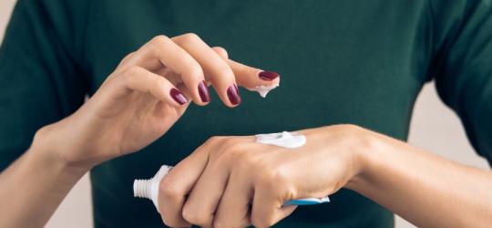 Kobieta smaruje dłonie kremem z mocznikiem.