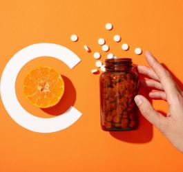 Osoba sięga po buteleczkę zawierającą suplement witaminy C.