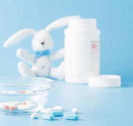 Na pierwszym planie tabletki, w tle maskotka królika z pustą butelką po lekach.