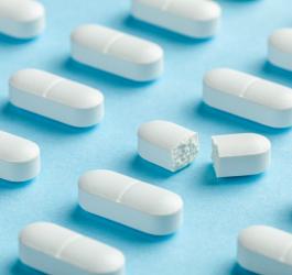 Białe tabletki z podziałką ułożone w równych rzędach. Jedna z tabletek jest przełamana.