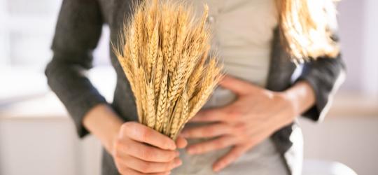 Kobieta trzyma w ręce kłosy pszenicy, cierpi na nietolerancję glutenu.