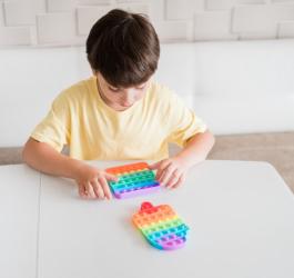 Chłopiec siedzi przy stole, bawi się kolorową zabawką.