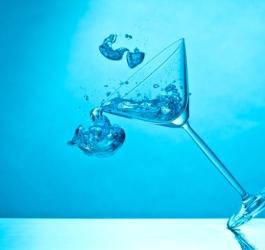 Błękitne tło. Kieliszek z alkoholem przewraca się, zawarty w nim napój wylewa się.