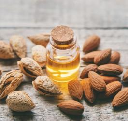 Buteleczka oleju ze słodkich migdałów oraz obrane i nieobrane migdały na drewnianym blacie.