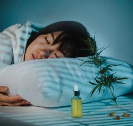 Kobieta śpi, obok leży buteleczka z olejkiem CBD, kapsułki oraz gałązka konopi siewnej.