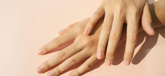 Zadbane, kobiece dłonie na różowym tle.