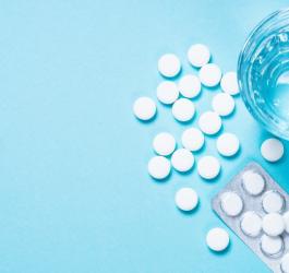 Blister, białe tabletki i szklanka wody na błękitnym tle.