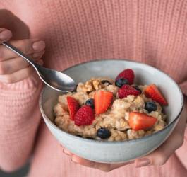 Kobieta trzyma w dłoni miskę z owsianką, z dodatkiem świeżych owoców.