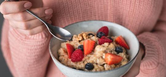 Kobieta trzyma w dłoni miskę z owsianką, z dodatkiem świeżych owoców.