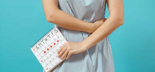 Kobieta odczuwa ból podbrzusza, w ręce trzyma kalendarz swojego cyklu menstruacyjnego i owulacji.