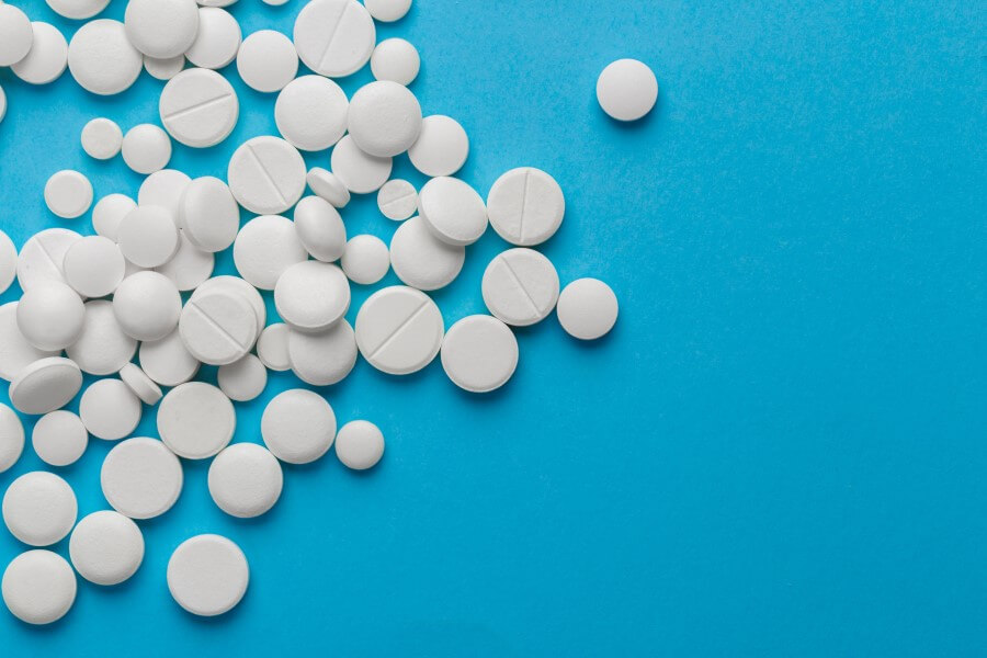 Białe tabletki różnych rozmiarów rozsypane na niebieskim tle.