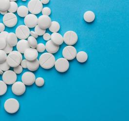 Białe tabletki różnych rozmiarów rozsypane na niebieskim tle.