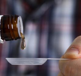 Mężczyzna nalewa na łyżeczkę syrop leczniczy.