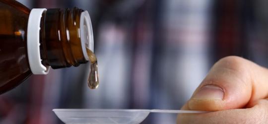 Mężczyzna nalewa na łyżeczkę syrop leczniczy.