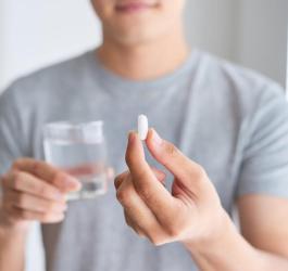 Mężczyzna trzyma szklankę wody i tabletkę paracetamolu.