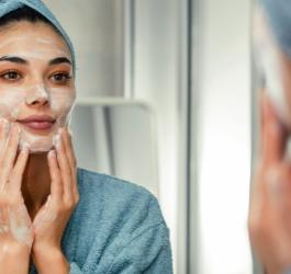 Kobieta wykonuje przed lustrem peeling enzymatyczny twarzy.