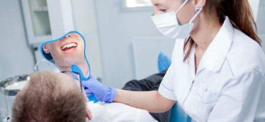 Pacjent u stomatologa, po piaskowaniu zębów ogląda efekty czyszczenia w lusterku.