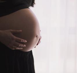 Kobieta w czarnej spódnicy i bluzce odsłaniającej ciążowy brzuch.