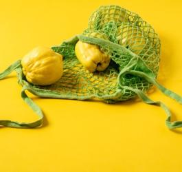 Żółte tło. Owoce pigwy wysypujące się z zielonej, siateczkowej torby na zakupy.