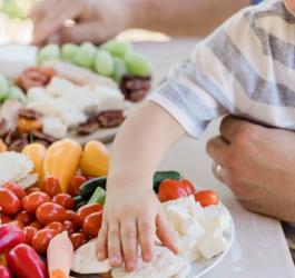 Dziecko siedzi przy stole, wybiera świeże warzywa i owoce.