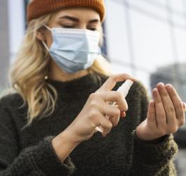 Kobieta w maseczce używa płynu do dezynfekcji dłoni.