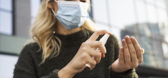 Kobieta w maseczce używa płynu do dezynfekcji dłoni.