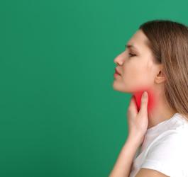 Kobieta chwyta się za szyję, cierpi na poporodowe zapalenie tarczycy.