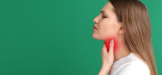 Kobieta chwyta się za szyję, cierpi na poporodowe zapalenie tarczycy.