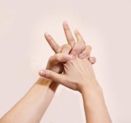 Kobiece dłonie splecione na różowym tle. Przestrzeń między palcami swędzi z powodu potnicy dłoni.